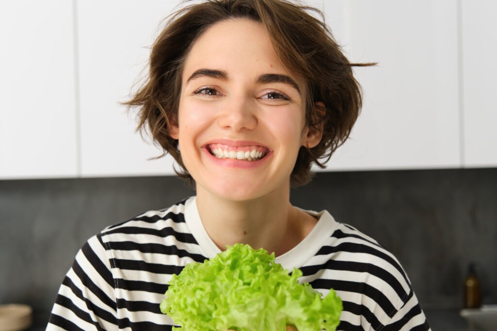 Smiling woman with green lettuce, representing food good for teeth in Brentwood.