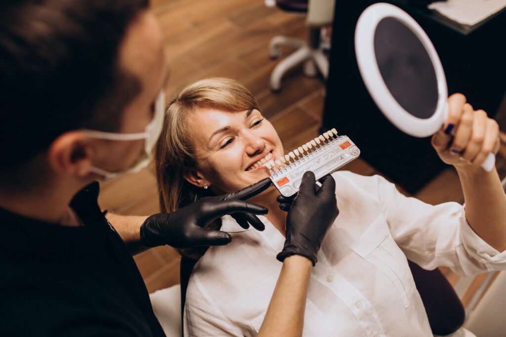A dentist shows a teeth shade guide to a smiling woman patient, reflecting the possibilities of Celebrity Dental Transformations in Brentwood.