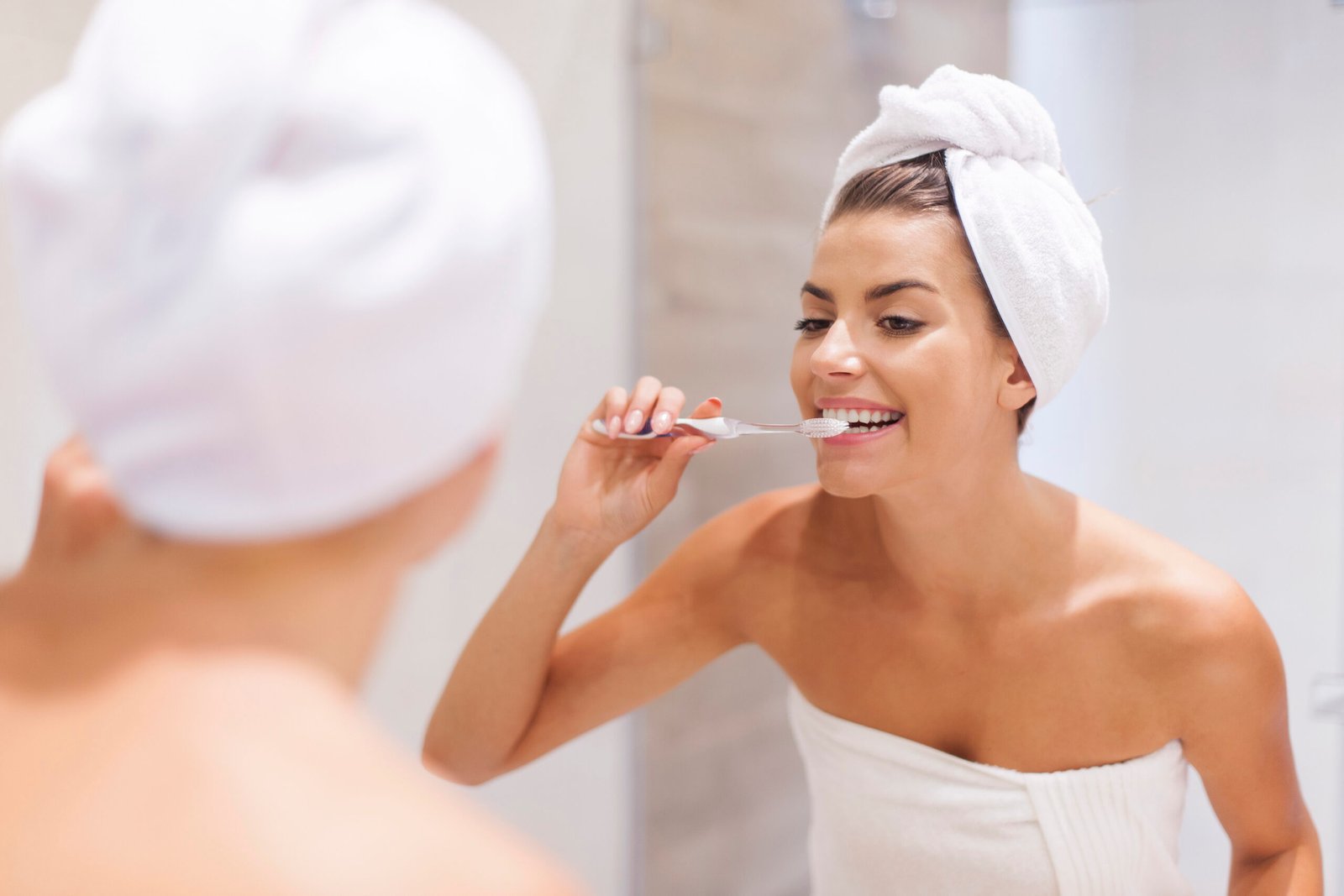 A young woman brushes her teeth, illustrating the importance of gentle technique to avoid harder brushing and protect oral health.